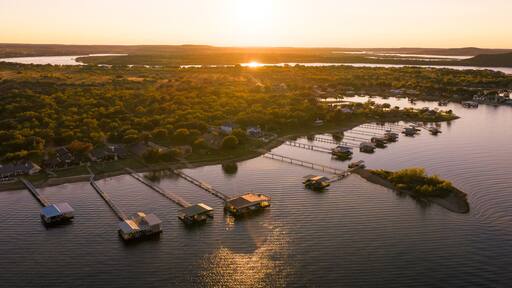 Aerial view of stilt houses stretch into the calm waters as the sun dips below the horizon, casting a warm glow over Possum Kingdom Lake, Possum Kingdom, Texas, United States.
