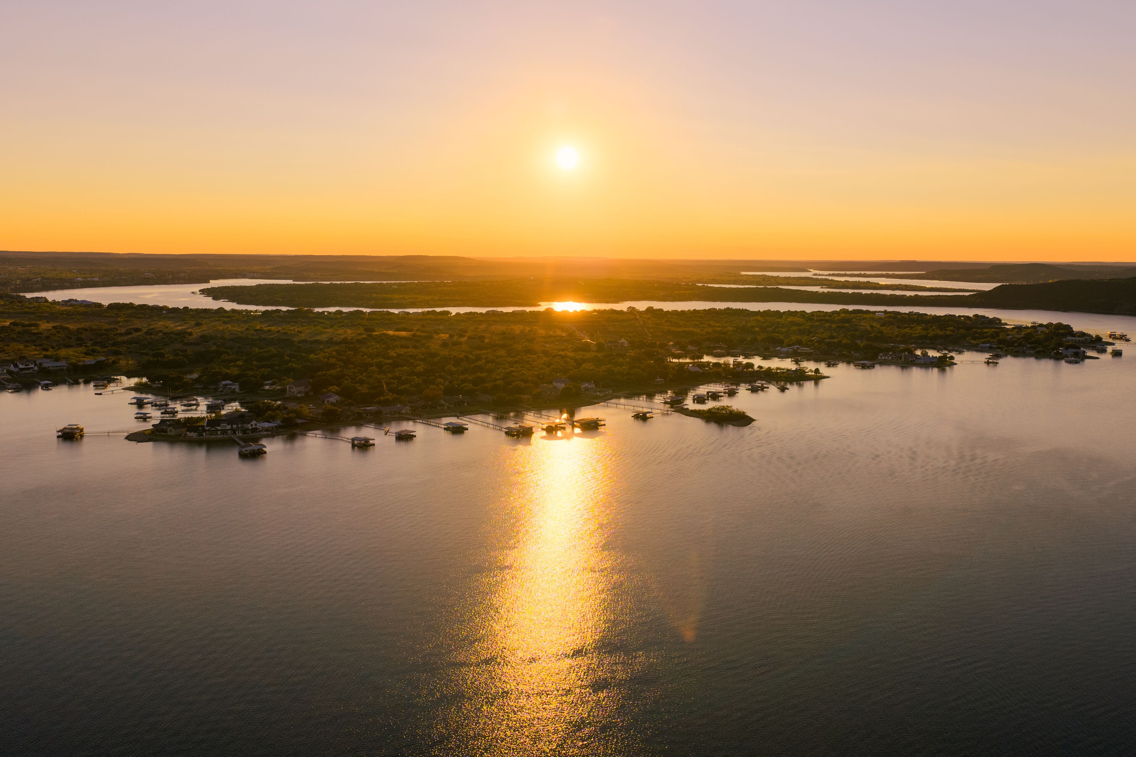 Aerial view of the sun's golden embrace over the tranquil lake waters, reflecting a shimmering path towards the horizon, Possum Kingdom, Texas, United States.