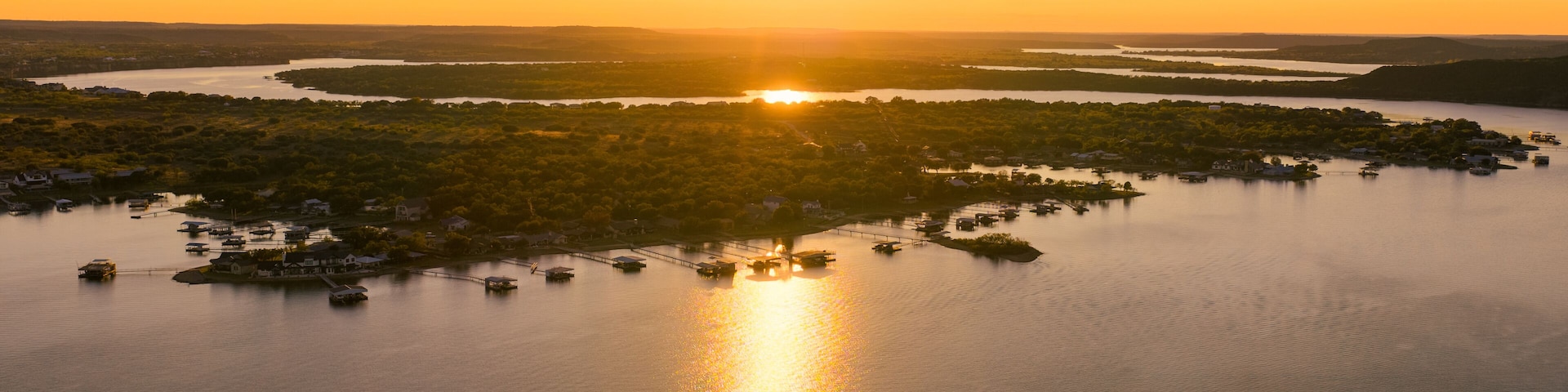 Aerial view of the sun's golden embrace over the tranquil lake waters, reflecting a shimmering path towards the horizon, Possum Kingdom, Texas, United States.
