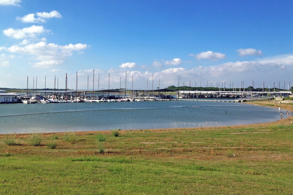 Un port de plaisance avec des bateaux amarrés, un champ verdoyant et un ciel bleu dégagé.