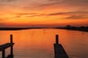 A breathtaking sunset casts a warm, orange glow over a calm river at Surfside Beach, Texas. The sky is painted with vibrant hues of orange and pink as the sun dips below the horizon.