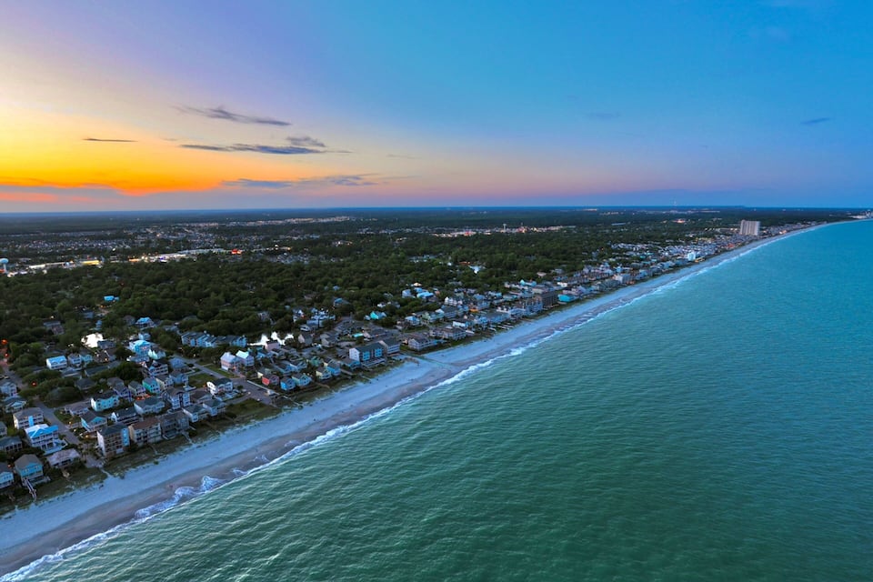 A coastal town at sunset with a beach, houses, and a clear sky.