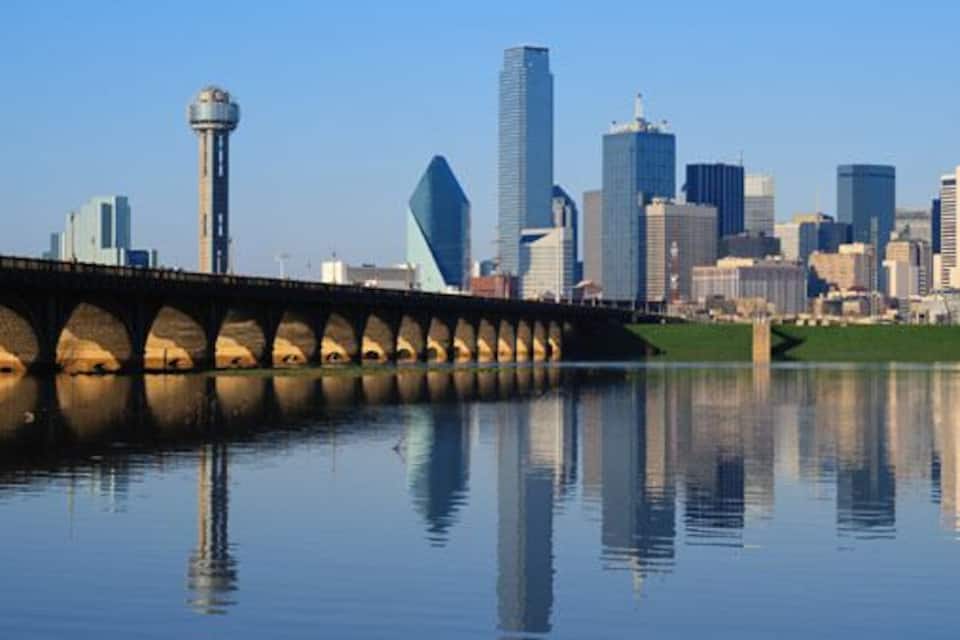 A city skyline with modern skyscrapers, a bridge over a calm river, and a prominent tower.