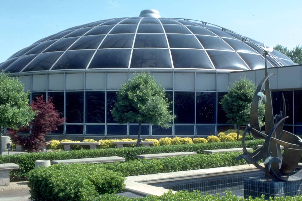 A large glass-domed building surrounded by well-maintained landscaping and a sculpture.