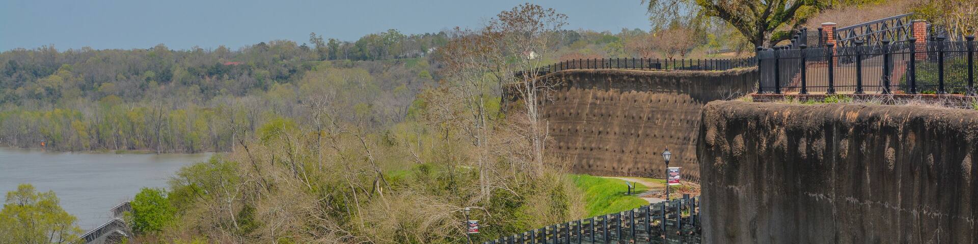 A concrete dam with a metal fence, a bridge, and a river.