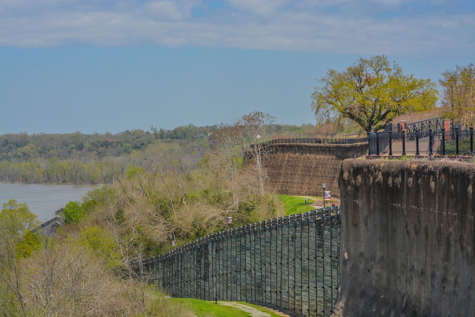 A concrete dam with a metal fence, a bridge, and a river.