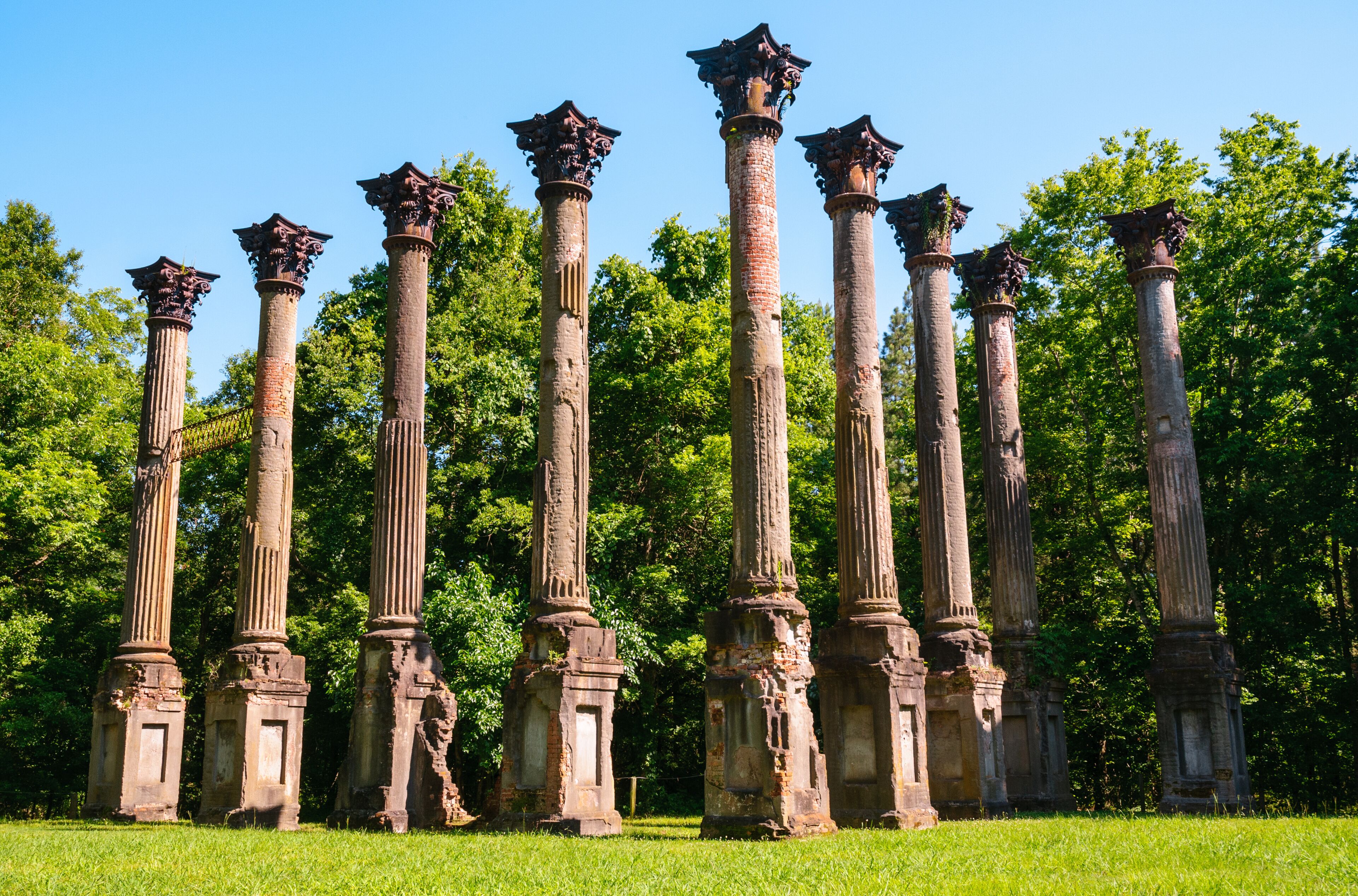 Ancient stone columns with capitals, set in a grassy area with trees in the background.