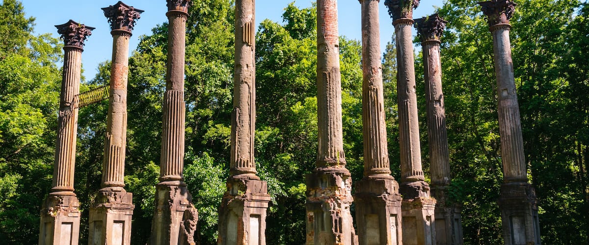 Ancient stone columns with capitals, set in a grassy area with trees in the background.