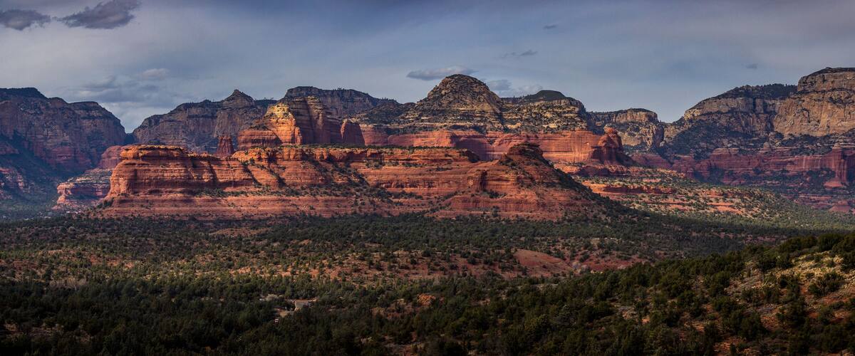 A rugged mountain range with prominent red rock formations and dense forested areas.