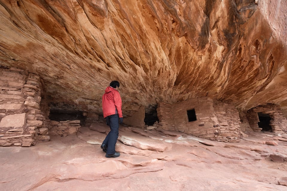 A person in a red jacket exploring an ancient stone structure with large rock formations overhead.
