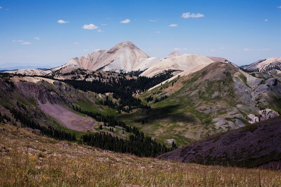A mountainous landscape with a prominent peak, forested valleys, and a clear blue sky.
