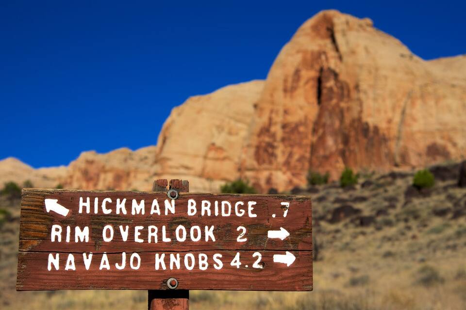 Un letrero de madera con indicaciones hacia el puente Hickman, el mirador del borde y los promontorios Navajo.