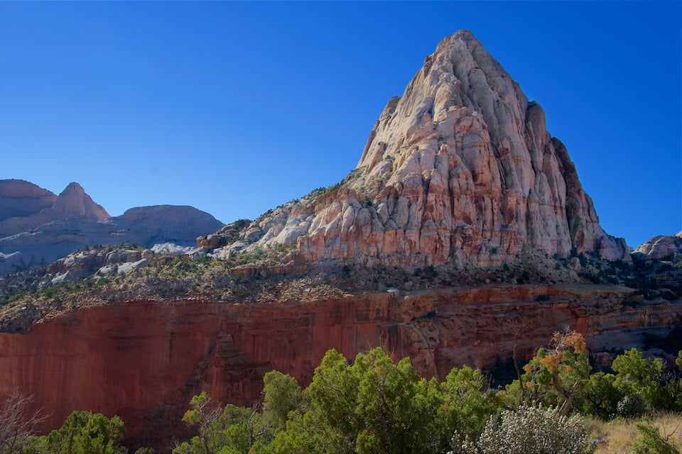 A prominent red rock formation with a peak, surrounded by green vegetation and other rocky mountains in the background.
