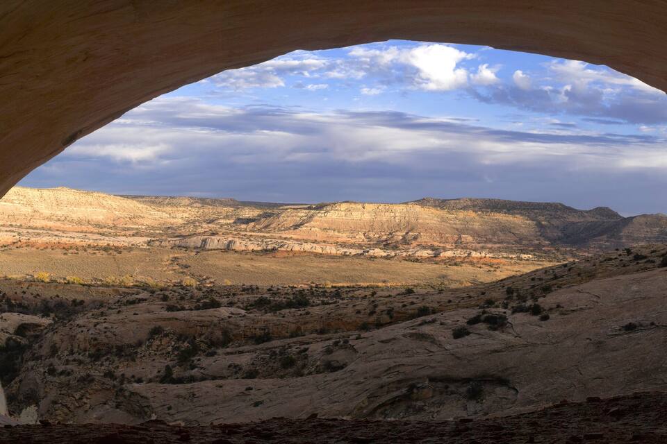 A natural rock arch with a view of a desert landscape and distant mountains.