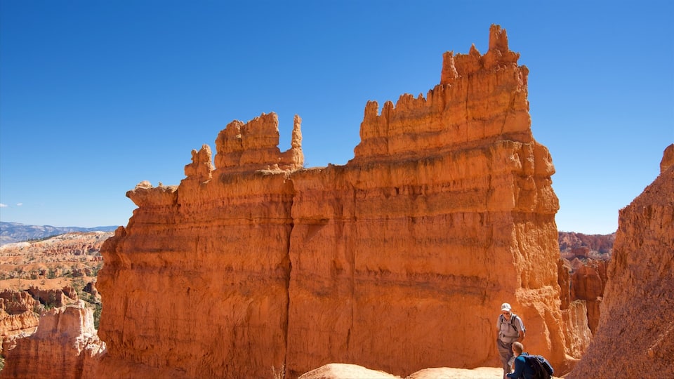 A large red rock formation with a person and a child standing in front.
