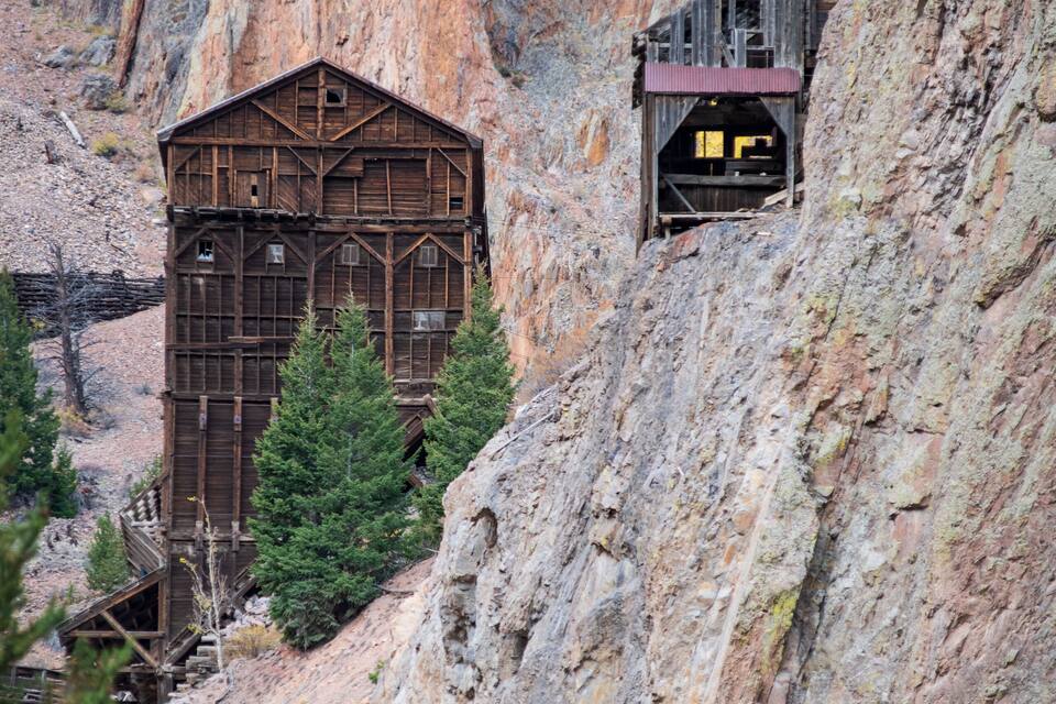 Un edificio de madera rústico ubicado en un cañón rocoso, con un camino de tierra que lo lleva hacia arriba.