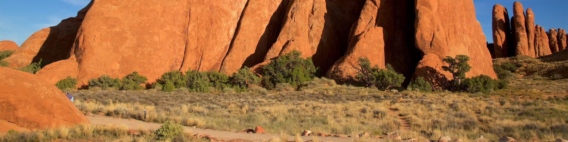 A landscape with large red rock formations and sparse vegetation under a clear blue sky.