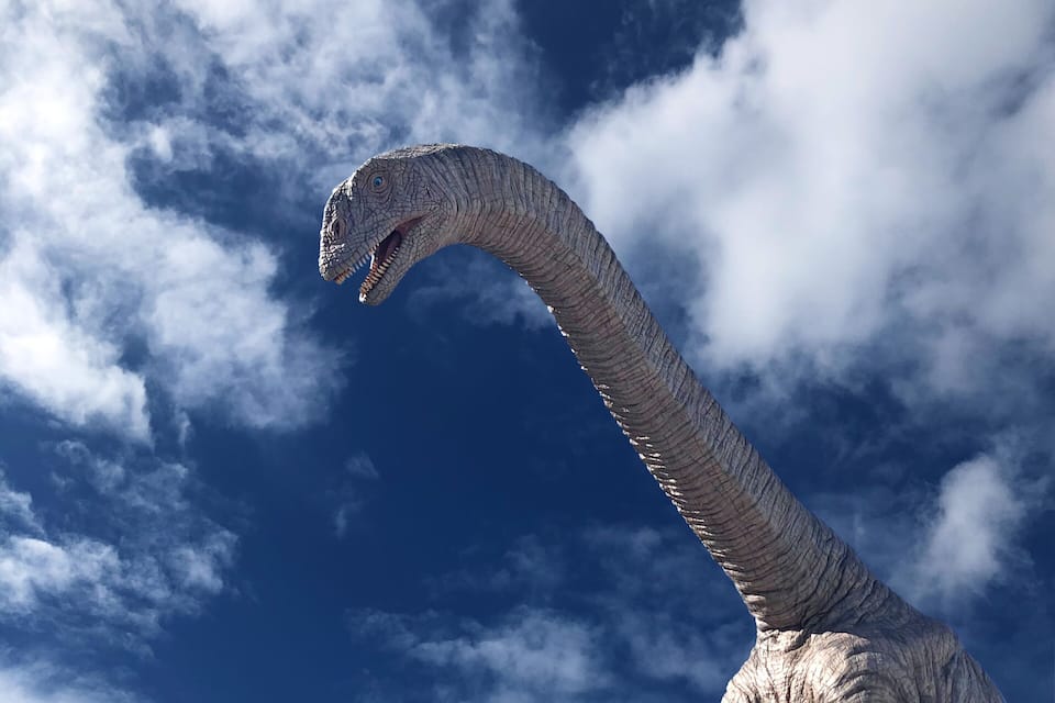 A dinosaur statue on a rock with a blue sky and clouds in the background.