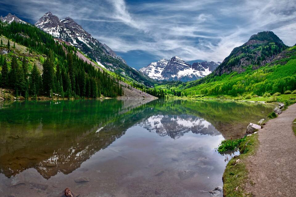 A mountain lake with reflections, surrounded by forested slopes and snow-capped peaks.