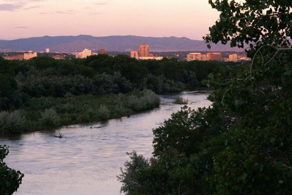 Un río serpenteando por una zona boscosa con edificios al fondo.