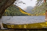 A yellow canoe tied to a tree by a calm lake with autumn-colored trees and mountains in the background.