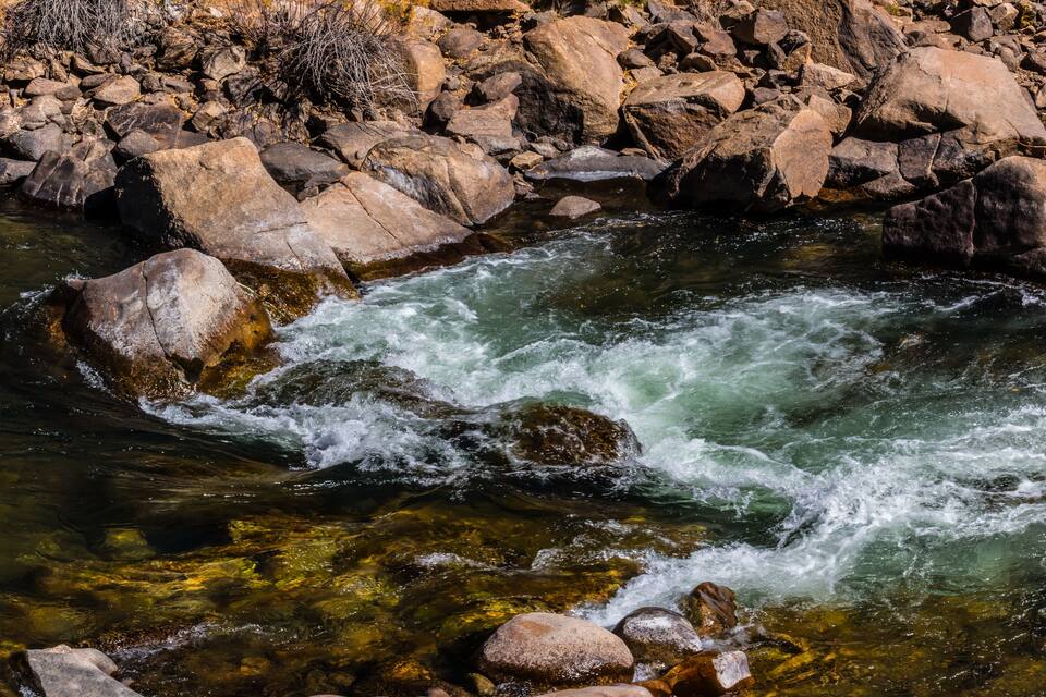 A fast-flowing river with clear water, surrounded by large rocks and boulders.
