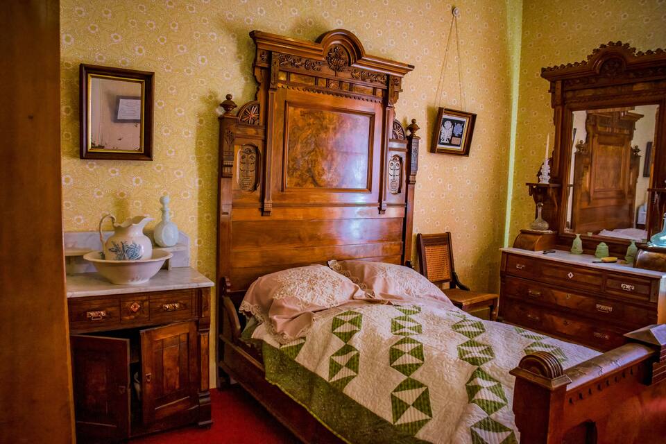A vintage bedroom with a wooden bed, a dresser, and a mirror.