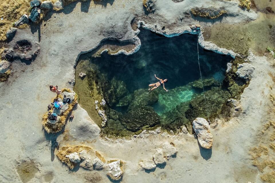 En vy från ovan av en klarblå pool omgiven av stenar och gles vegetation.