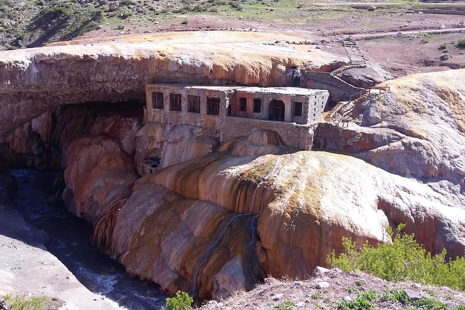 Estructura de piedra incrustada en un acantilado, con un río corriendo debajo.