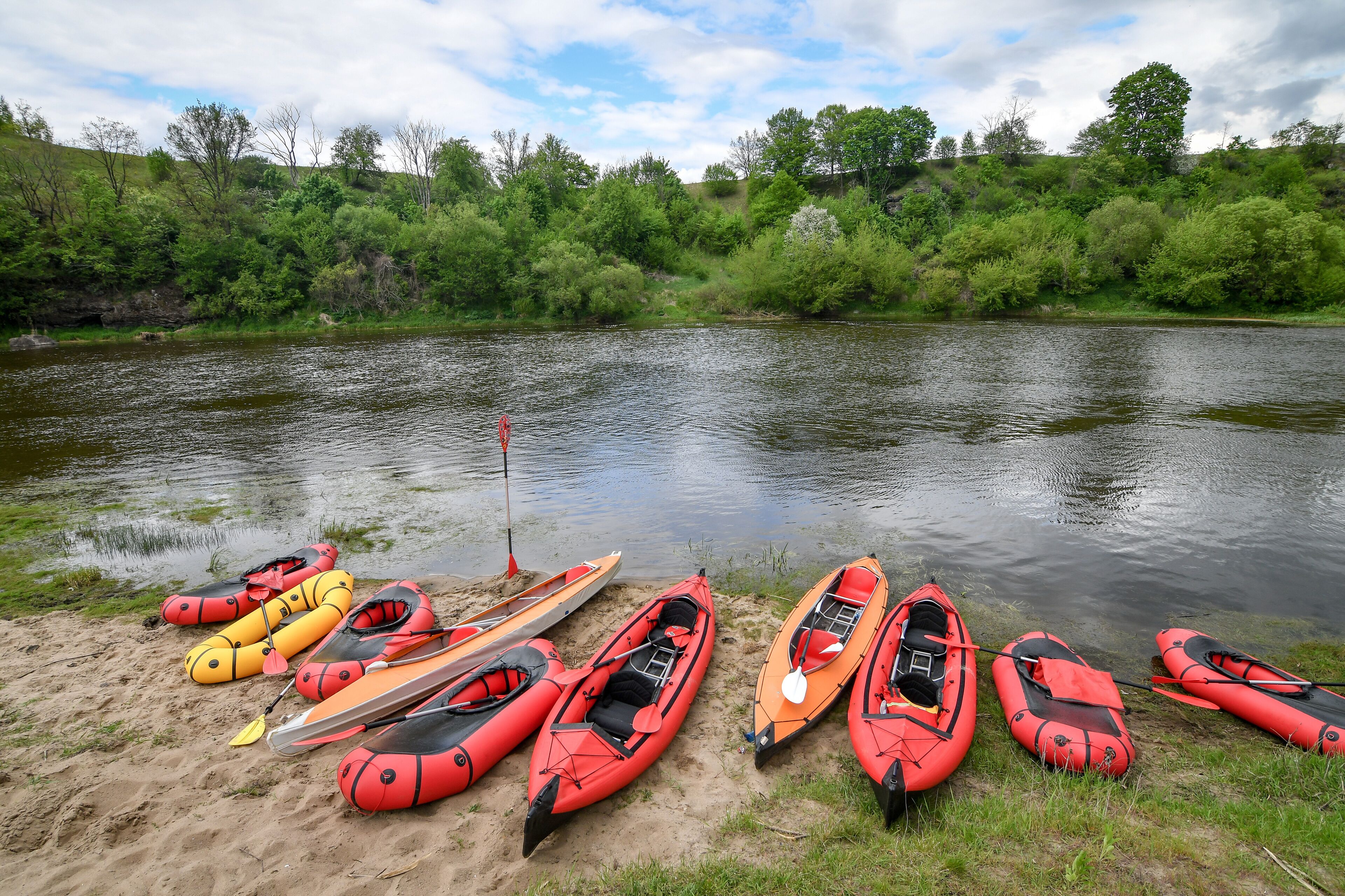 Packraft rubber boats and kayaks on sandy river bank, with dramatic sky. Selective focus. Active lifestyle concept.