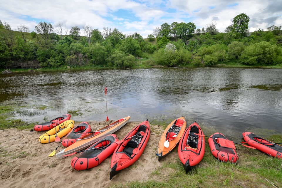 A riverbank with several kayaks and rafts lined up on the sand.
