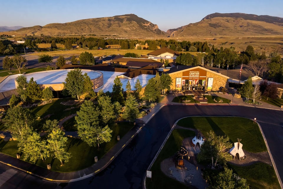 An aerial view of a town with a prominent building, a large parking lot, and surrounding hills.