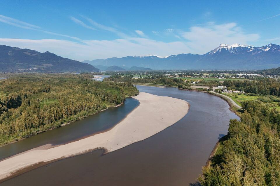 Um rio serpenteando por um vale arborizado, com montanhas ao fundo.