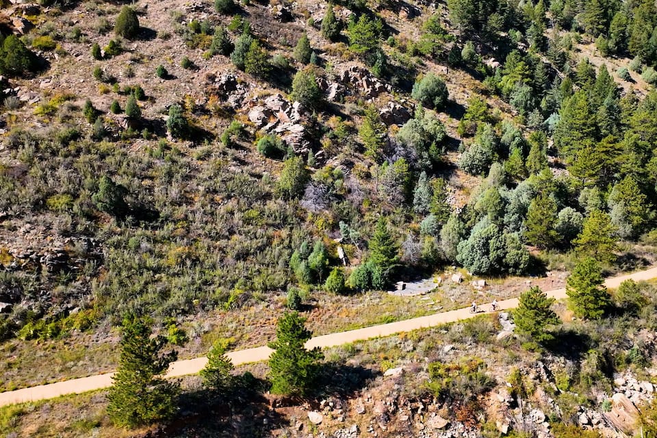 Paisagem montanhosa com florestas densas, terreno rochoso e uma trilha de terra.