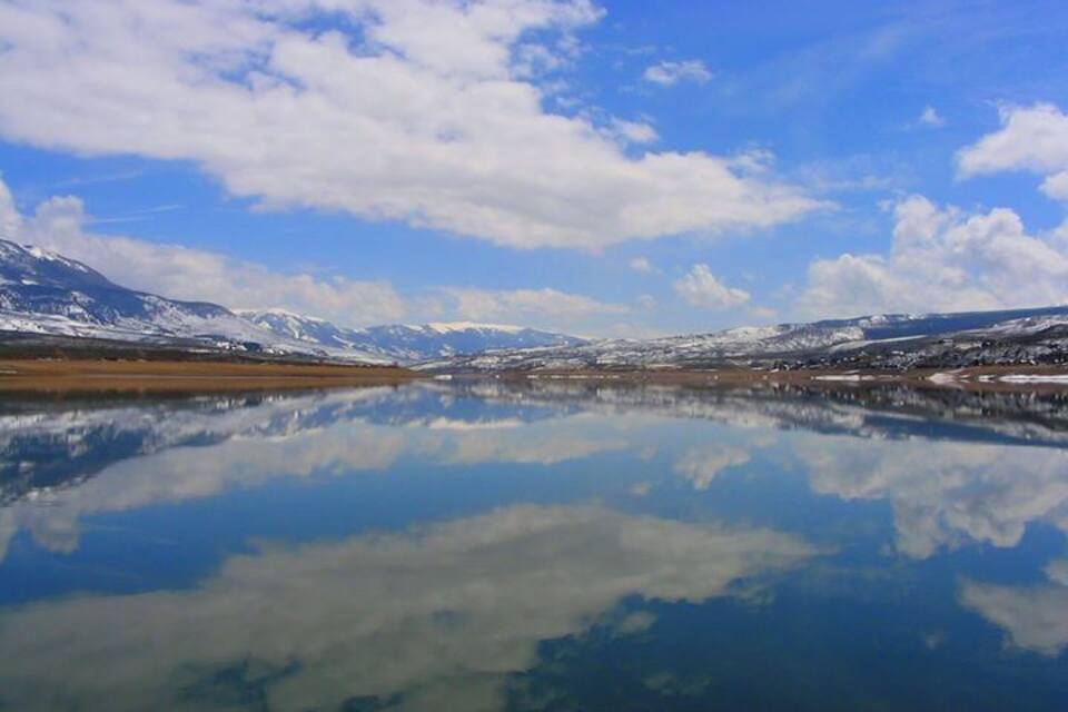 A calm lake reflecting snow-capped mountains and a clear blue sky.
