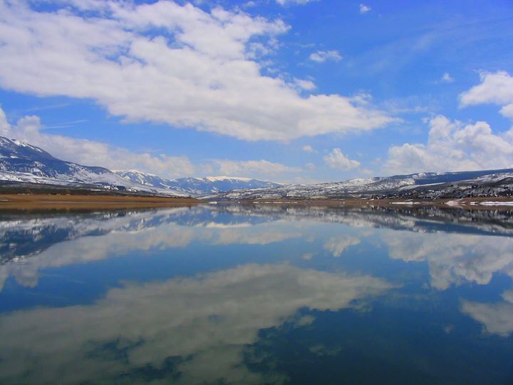 A calm lake reflecting snow-capped mountains and a clear blue sky.