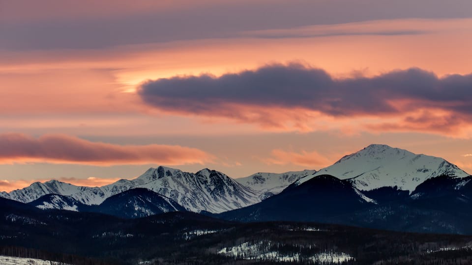 A mountain range with snow-capped peaks and a sunset sky.