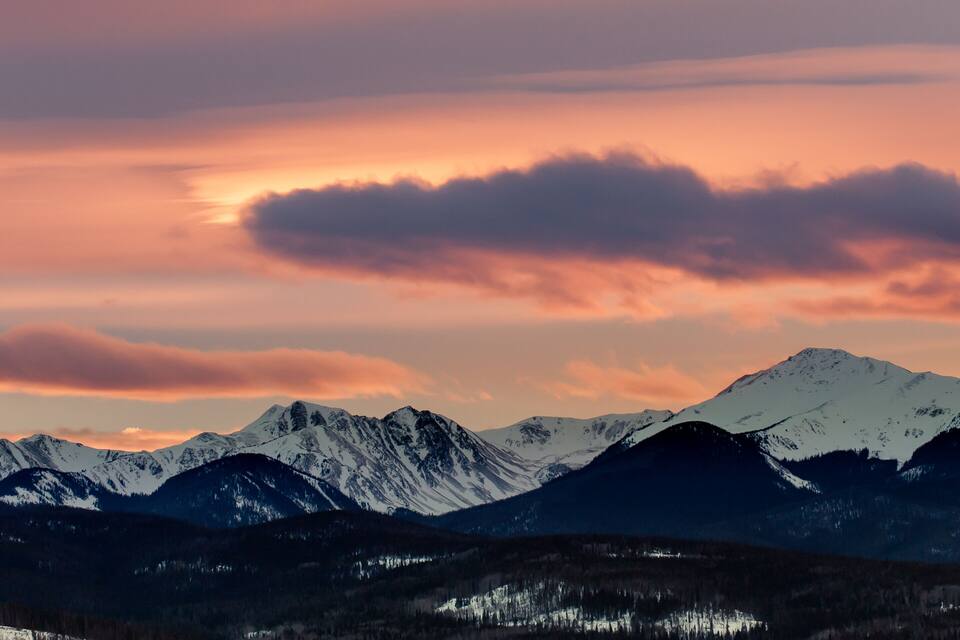 Une chaîne de montagnes aux sommets enneigés, sous un ciel embrasé par le coucher du soleil.