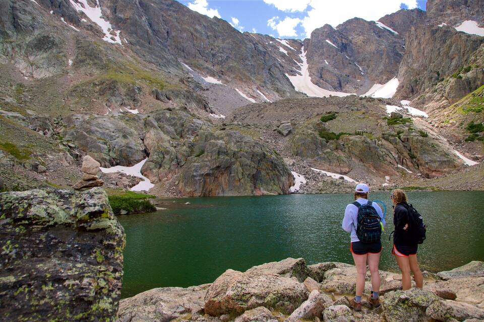 Un lago rocoso rodeado de montañas con parches de nieve.