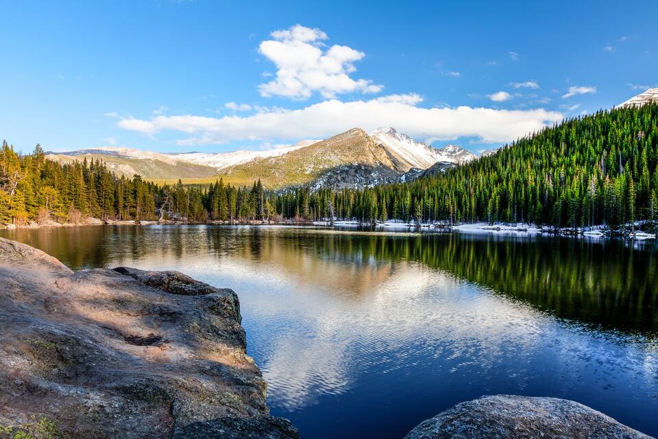 A calm lake surrounded by snow-capped mountains and dense evergreen forests.