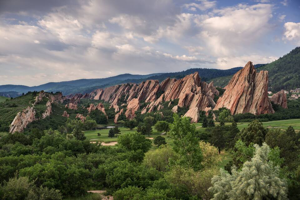 A mountainous landscape with prominent red rock formations and lush green trees.