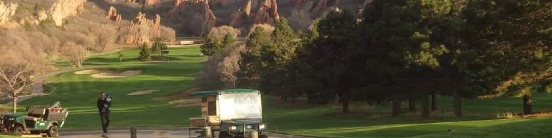 A golf course with a truck and a person walking on the road, surrounded by mountains and trees.