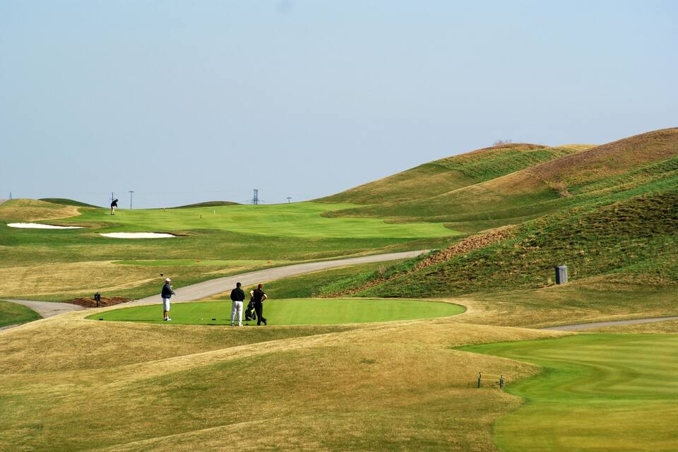 Um campo de golfe com colinas ondulantes, áreas de areia e céu limpo.