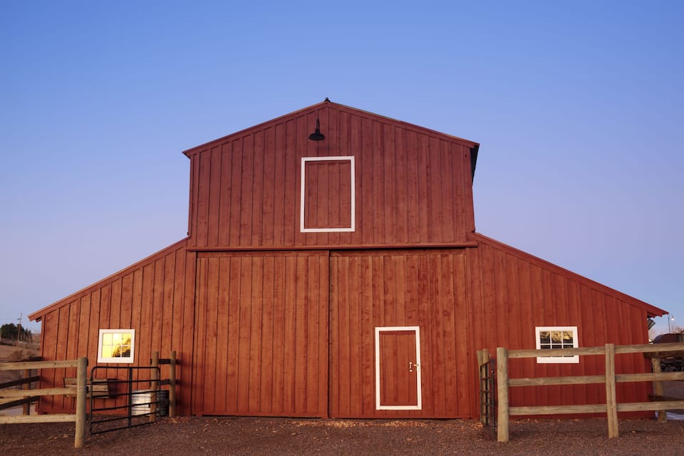A red barn with a white door and window frames, a metal gate, and a wooden fence.