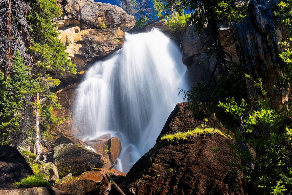 Uma cascata desce por um penhasco rochoso, rodeada por vegetação exuberante.