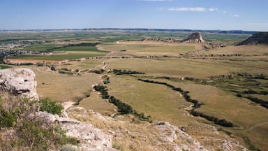 A vast landscape with rolling hills, a prominent rock formation, and a distant town.