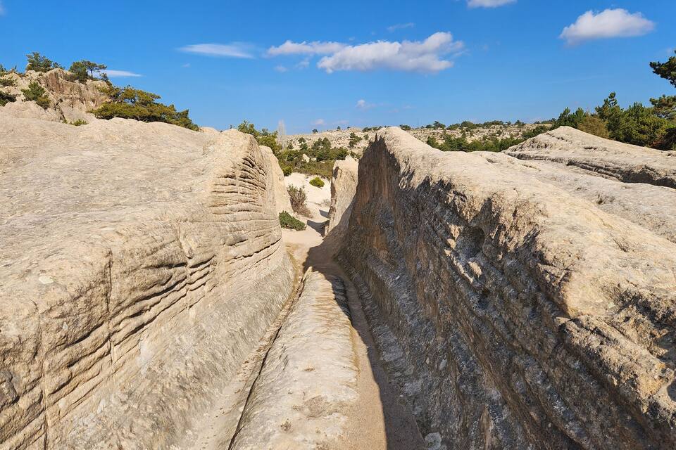A narrow canyon with layered rock formations and sparse vegetation.