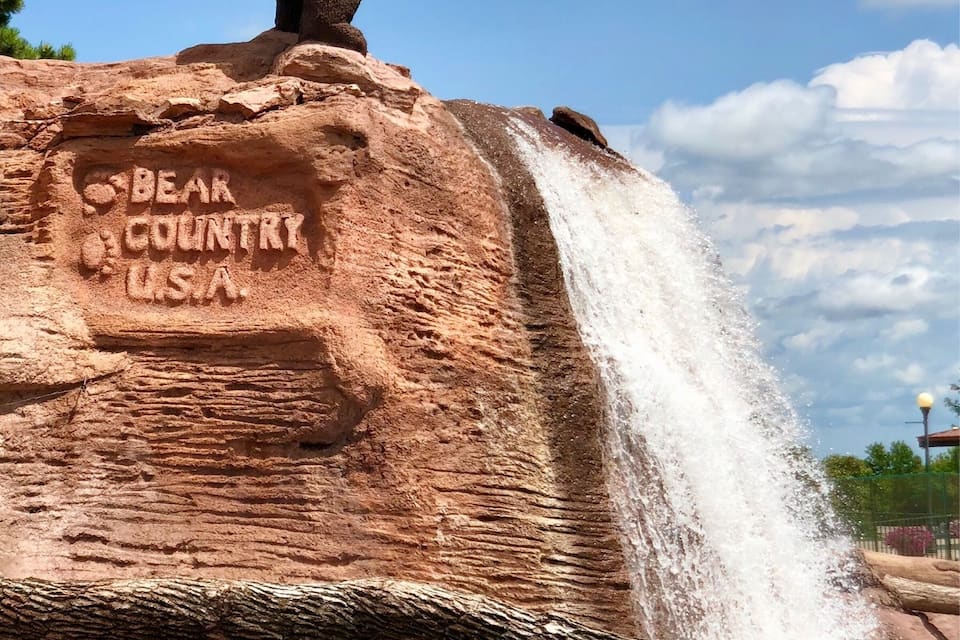 A bear sculpture on a rock with a waterfall and the words "Bear Country USA" carved into it.