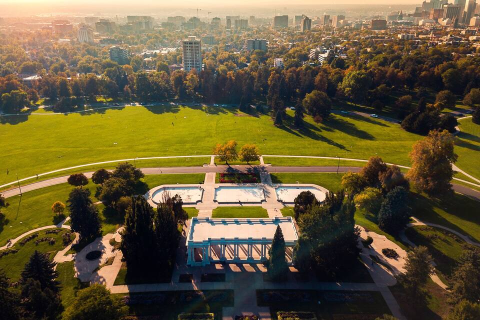 Ein Park mit einem Brunnen, umgeben von Bäumen und Gebäuden im Hintergrund.