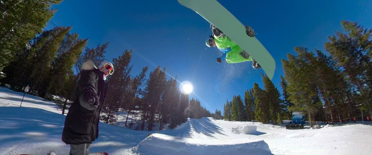 SELFIE: Woman takes a selfie while snowboarder jumps off kicker and does a trick